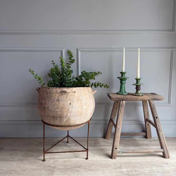 Decorative setup with a large planter, wooden stool, and candles against a gray wall.