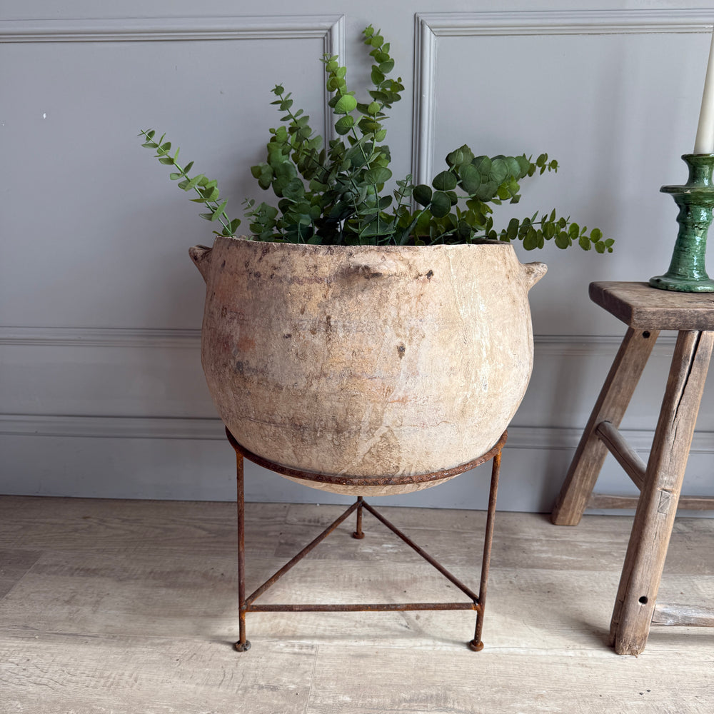Decorative pot with greenery on a stand against a gray wall