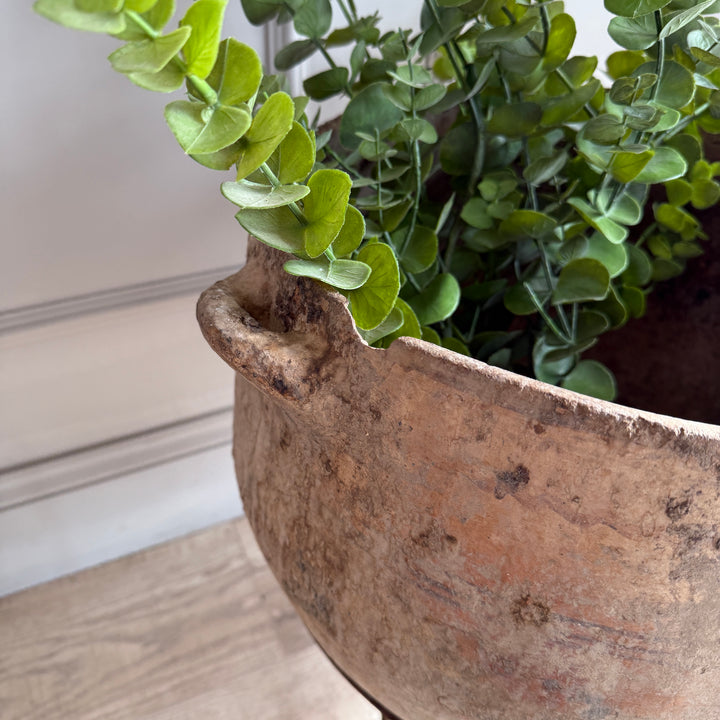 Artificial eucalyptus plant in a rustic pot on a wooden surface.