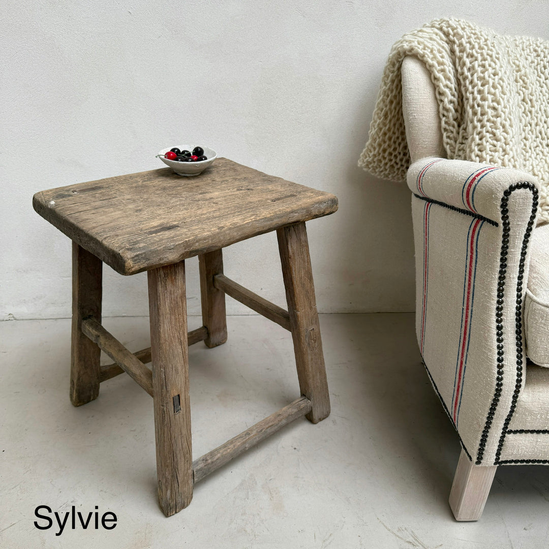Wooden side table next to a chair with a textured blanket in a minimalistic room.