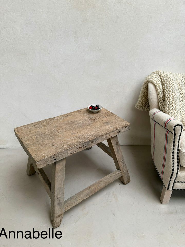Wooden table with a chair and blanket against a white wall, featuring the brand &