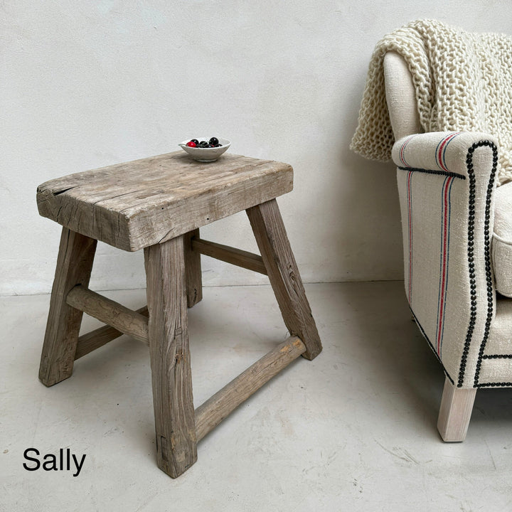 Wooden stool with a bowl of fruit next to a chair with a blanket on it, labeled &