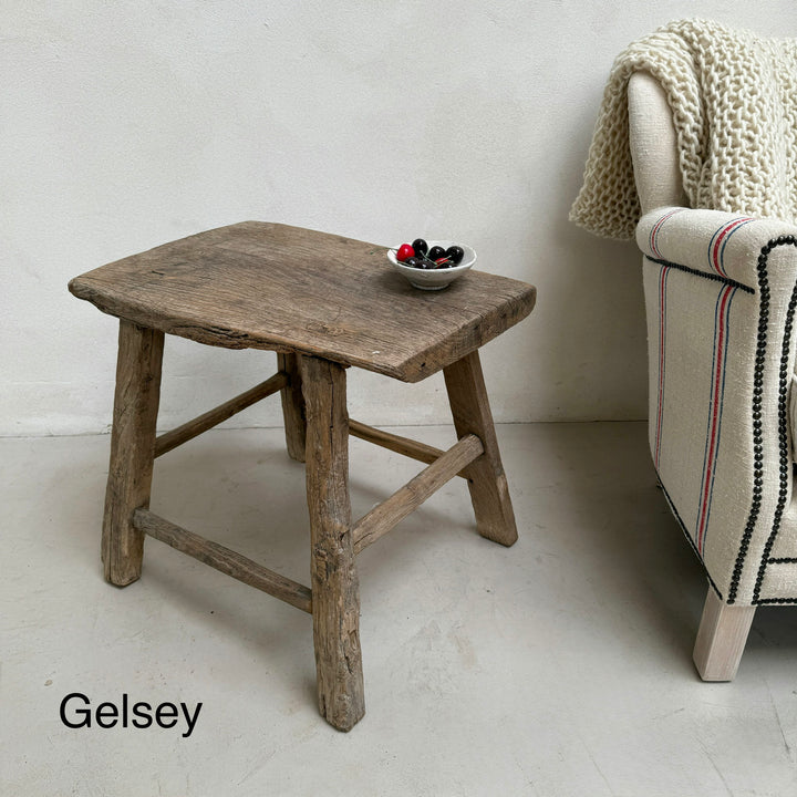 Wooden side table with a bowl of fruit next to a striped armchair against a white wall.