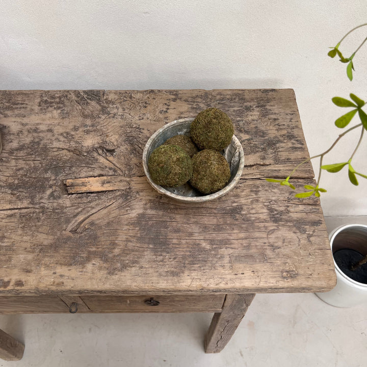 Three green mossy decorative balls displayed in a small rustic ceramic bowl on a weathered wooden table.