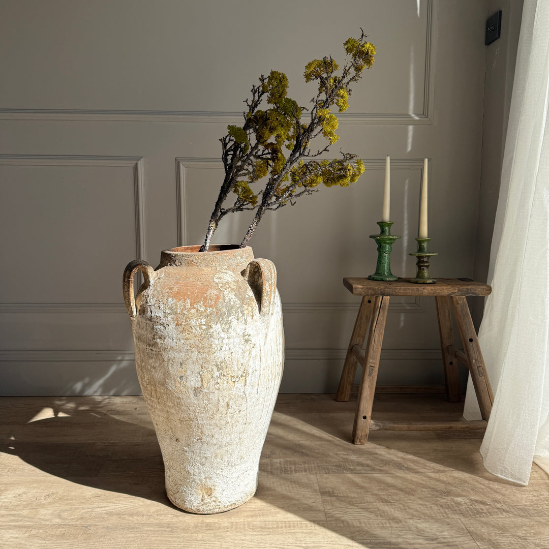 Decorative vase with dried flowers on a wooden floor next to a small wooden stool with candles.
