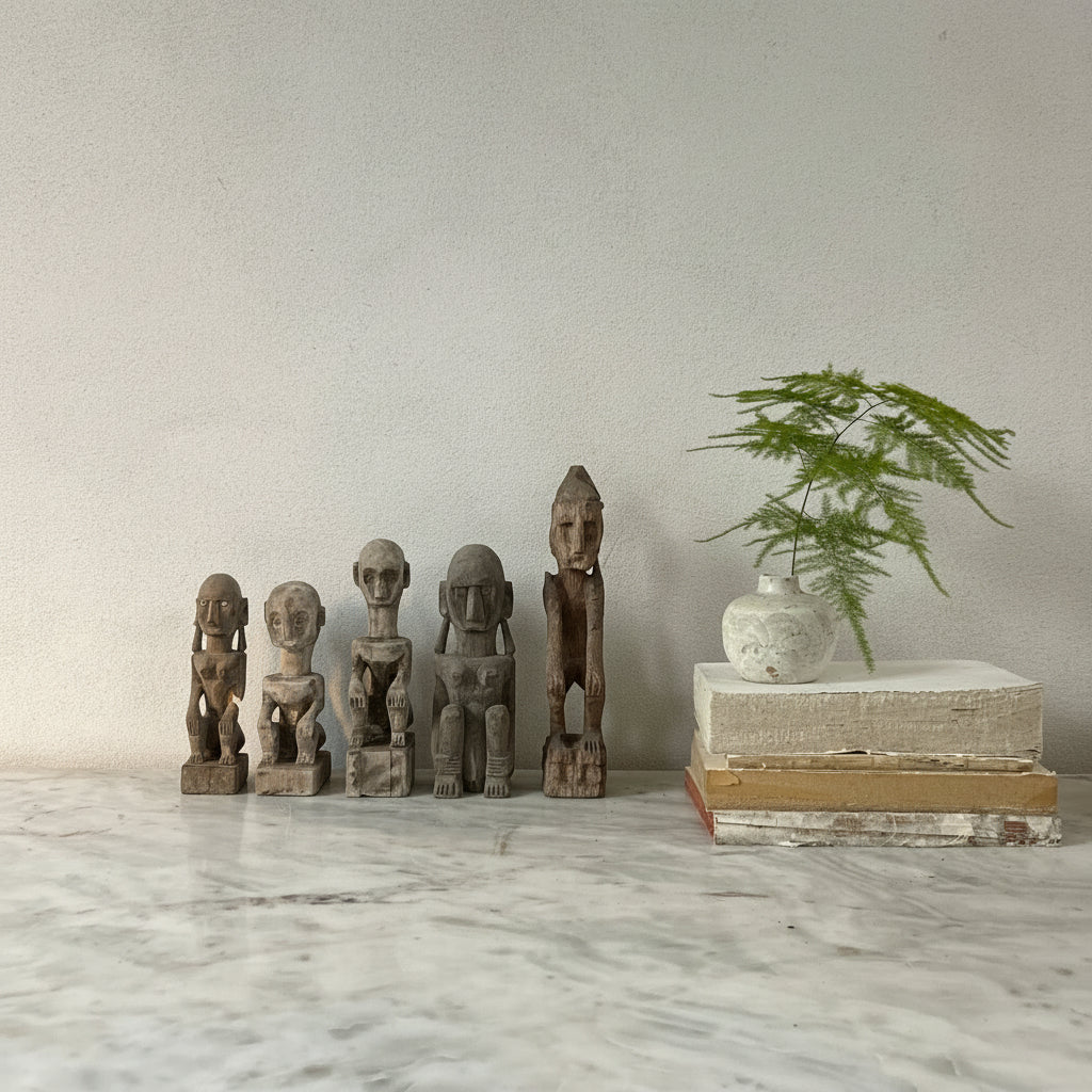Set of wooden sculptures on a marble surface with a plant and books in the background.