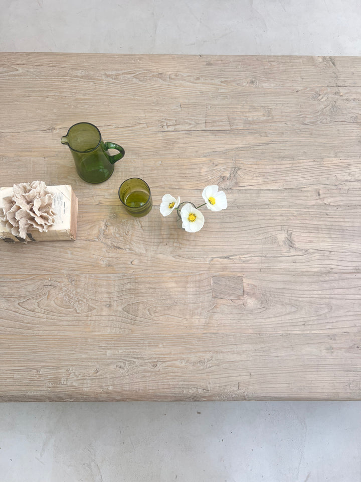 Wooden surface with decorative items including green glasses and white flowers on a light gray background