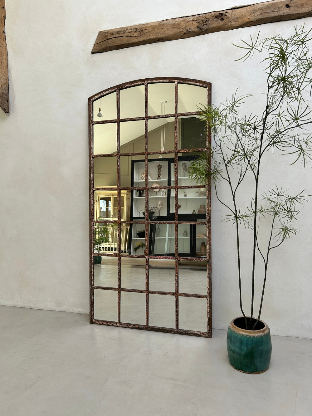 Large decorative mirror with a rustic frame in a room with a plant and wooden beam.