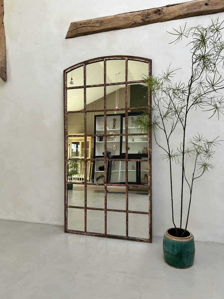 Large decorative mirror with a rustic frame in a room with a plant and wooden beam.