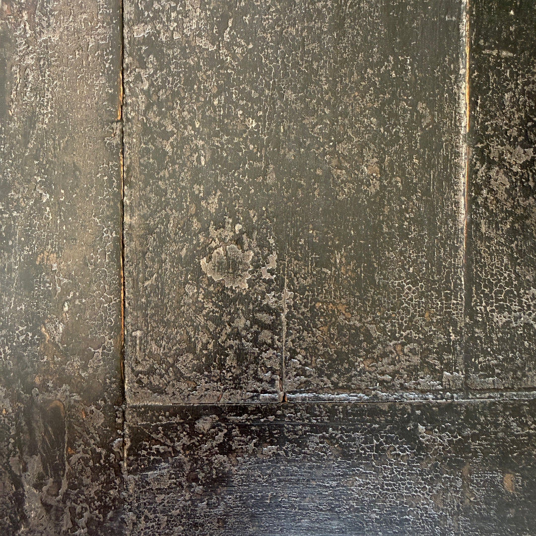A close-up of a dark, weathered wood surface with visible grain, peeling paint or finish, and vertical panel seams.
