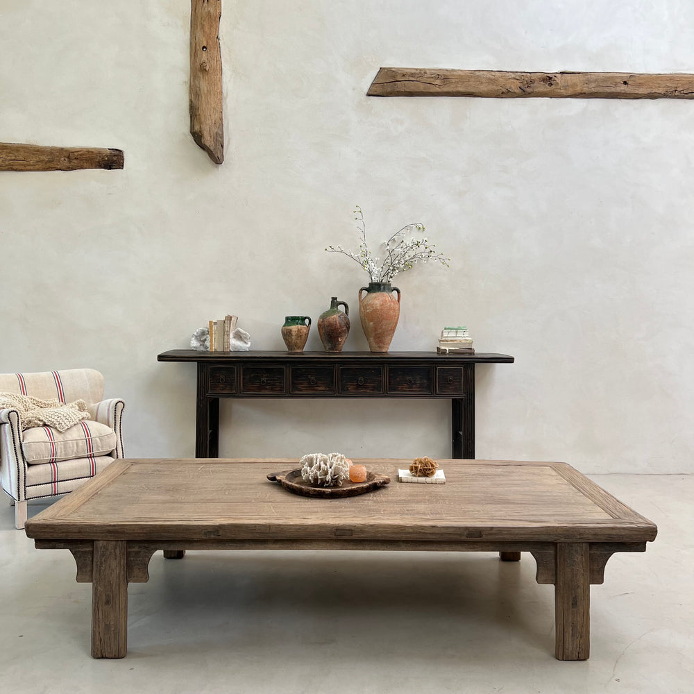 Wooden coffee table with decorative items in a room with a plaid armchair and rustic decor.