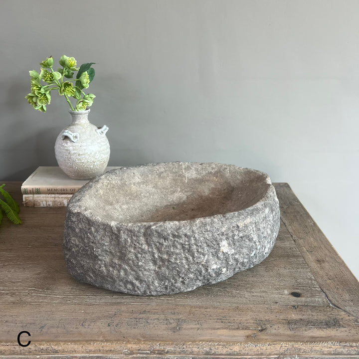Stone bowl on a wooden surface with a vase and plant in the background