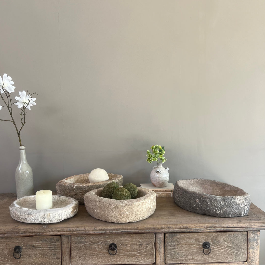 Set of stone bowls on a wooden dresser with decorative items against a plain wall.