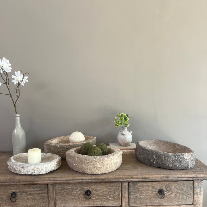 Set of stone bowls on a wooden dresser with decorative items against a plain wall.