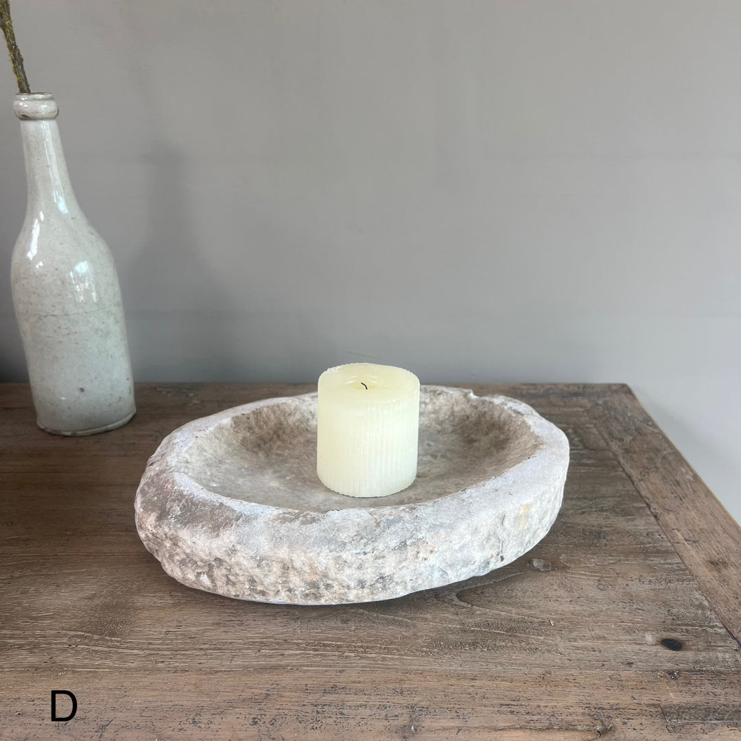 Candle in a stone bowl on a wooden surface with a white bottle in the background