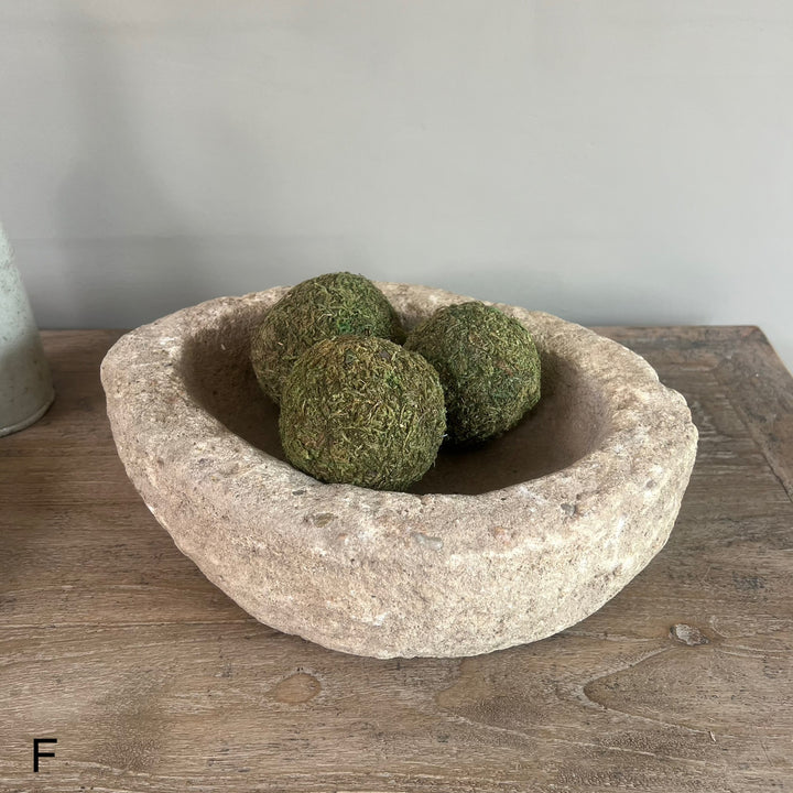 Decorative stone bowl with green spherical objects on a wooden surface