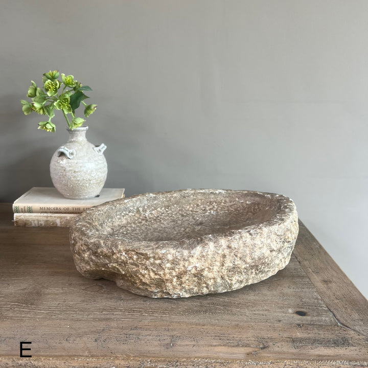 Decorative stone bowl on a wooden surface with a small vase and books in the background.