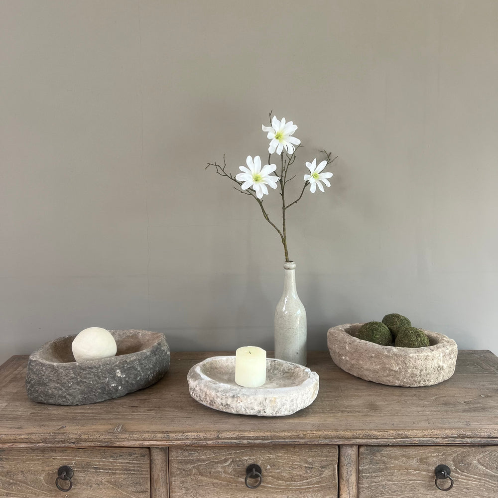 Decorative setting with stone bowls, a vase with flowers, and a candle on a wooden surface.