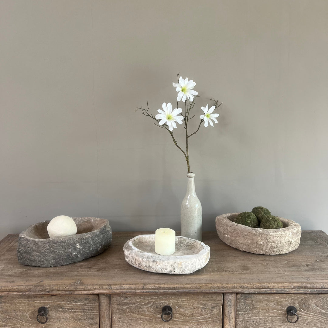 Decorative setting with stone bowls, a vase with flowers, and a candle on a wooden surface.
