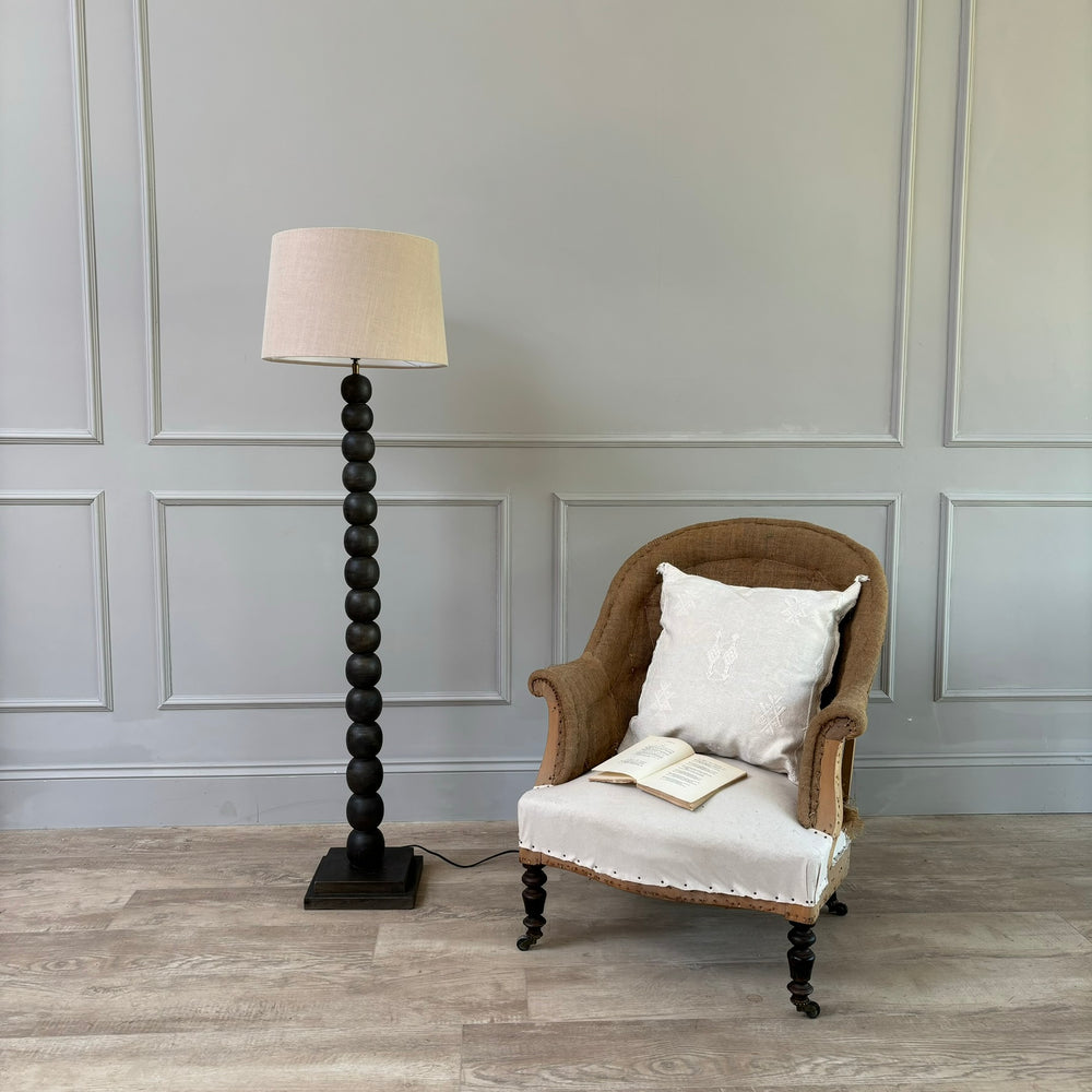 Bobbin floor lamp with shade next to a antique French armchair 