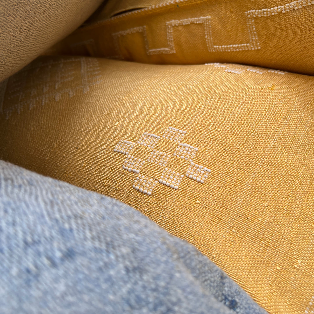 Close-up of beige fabric with embroidered design, partially overlapped by blue fabric.