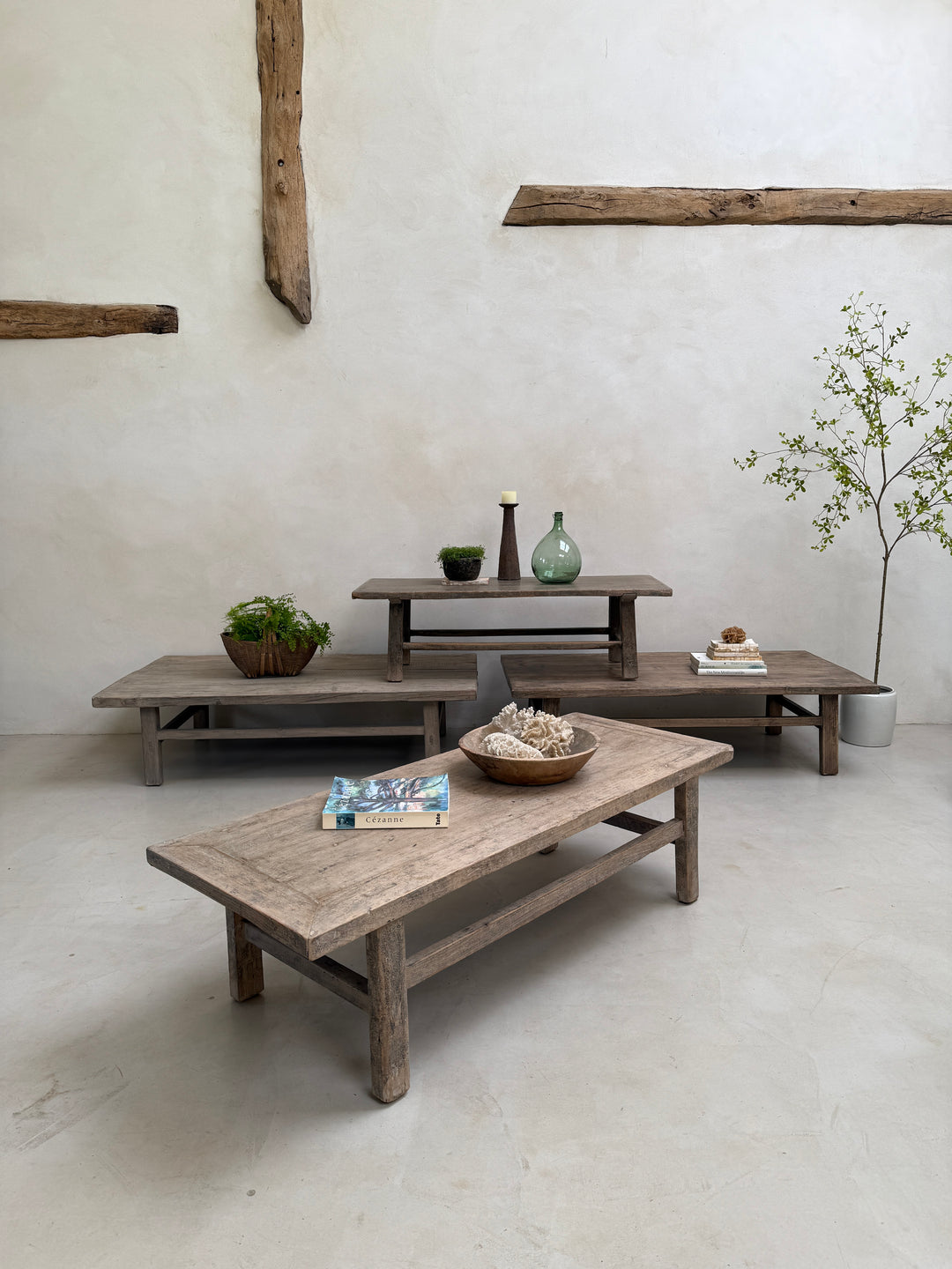 Set of wooden tables in a minimalistic room with plants and decor items.