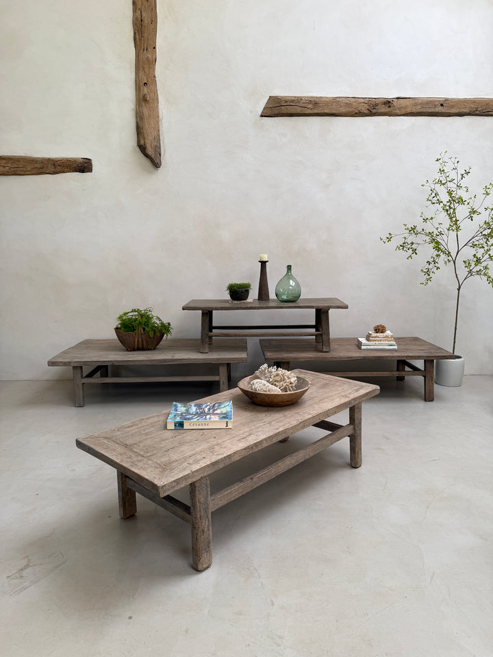 Set of wooden tables in a minimalistic room with plants and decor items.