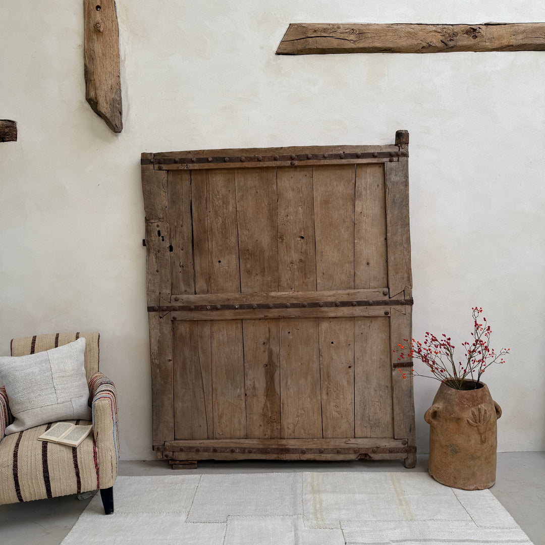 Vintage wooden wardrobe against a white wall with a chair and vase in the foreground.