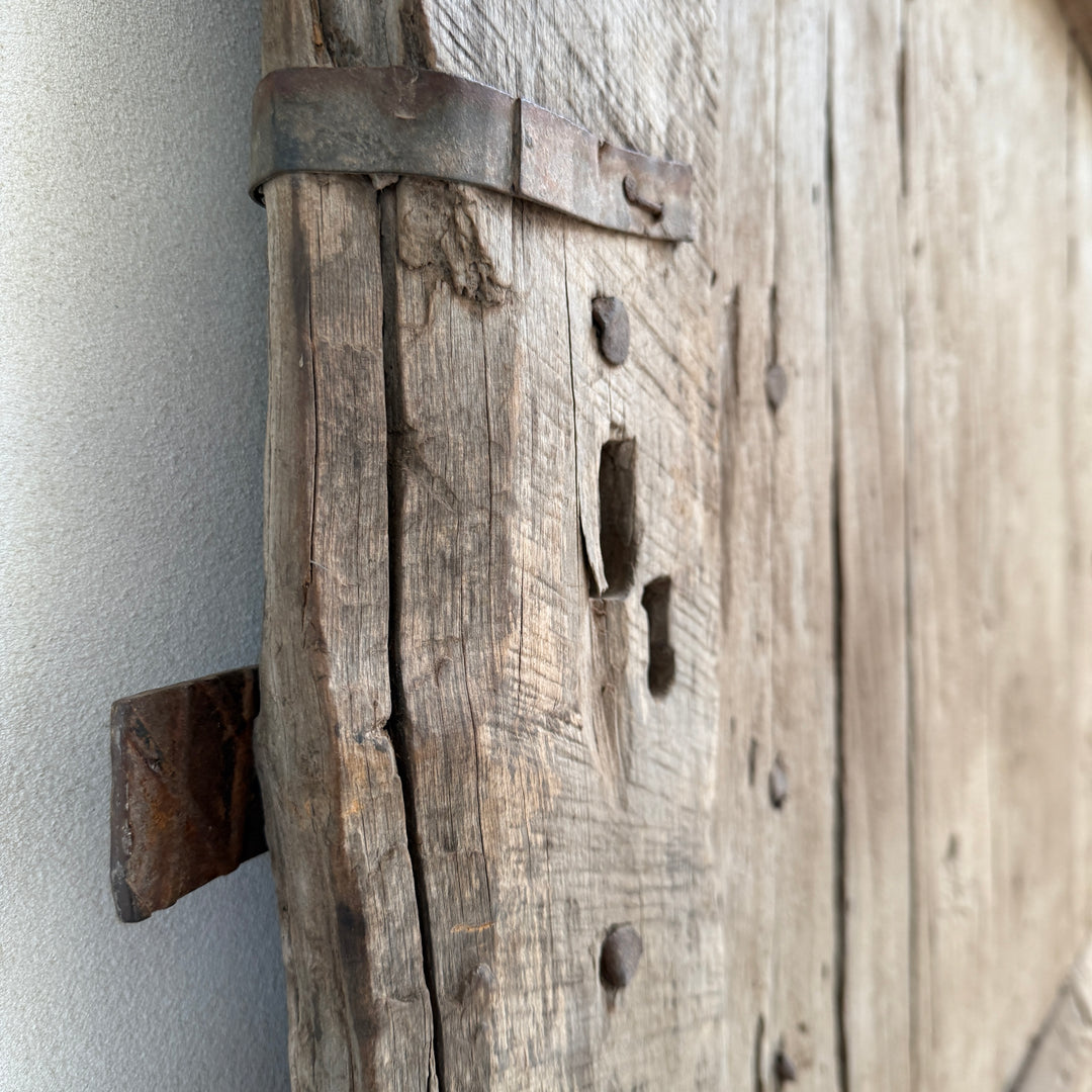 Close-up of a rustic wooden door with metal hardware against a neutral background
