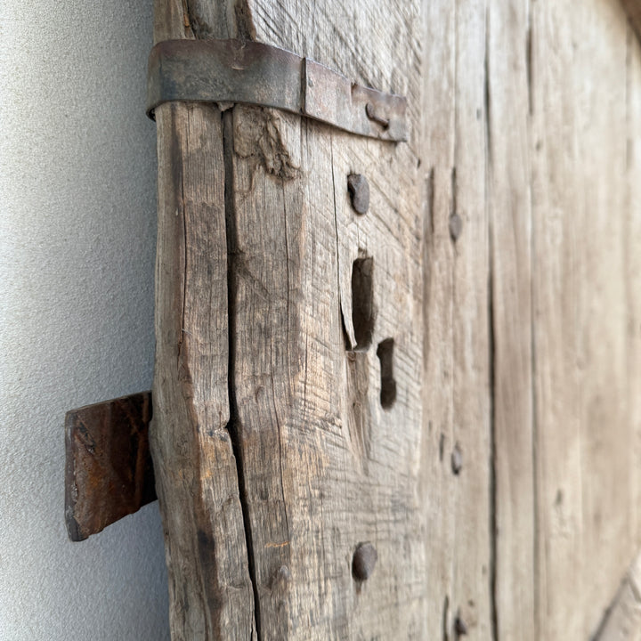 Close-up of a rustic wooden door with metal hardware against a neutral background