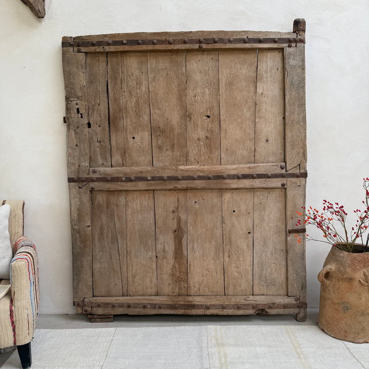 Vintage wooden cabinet against a white wall with a plant on the right.