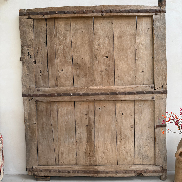 Large wooden door with a rustic appearance against a white wall.
