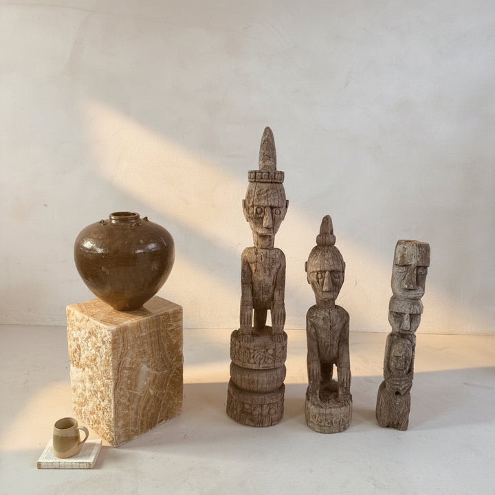 Three wooden statues and a black vase on a light gray surface with a neutral background