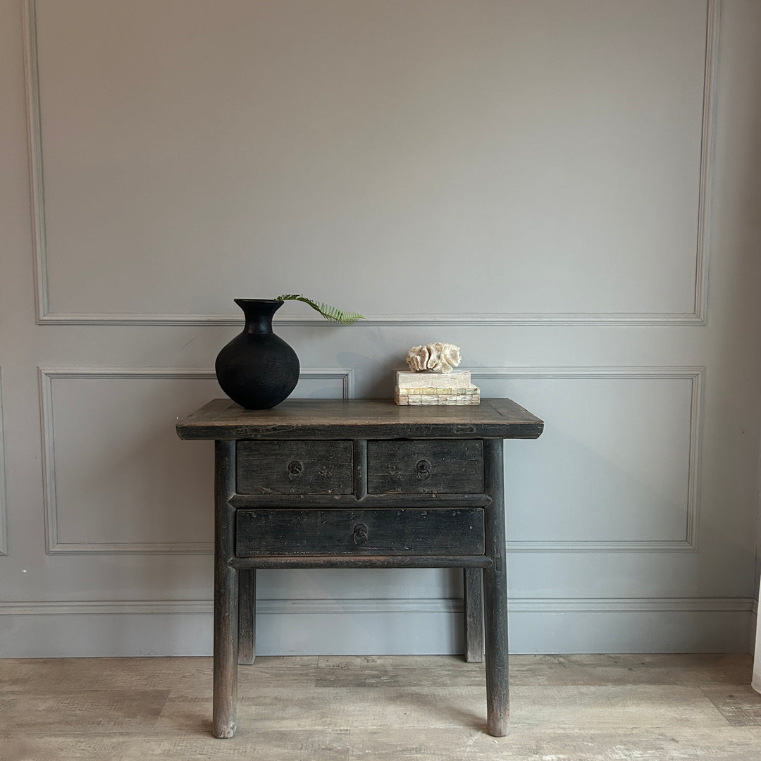 Vintage wooden side table with a black vase and books against a gray wall.