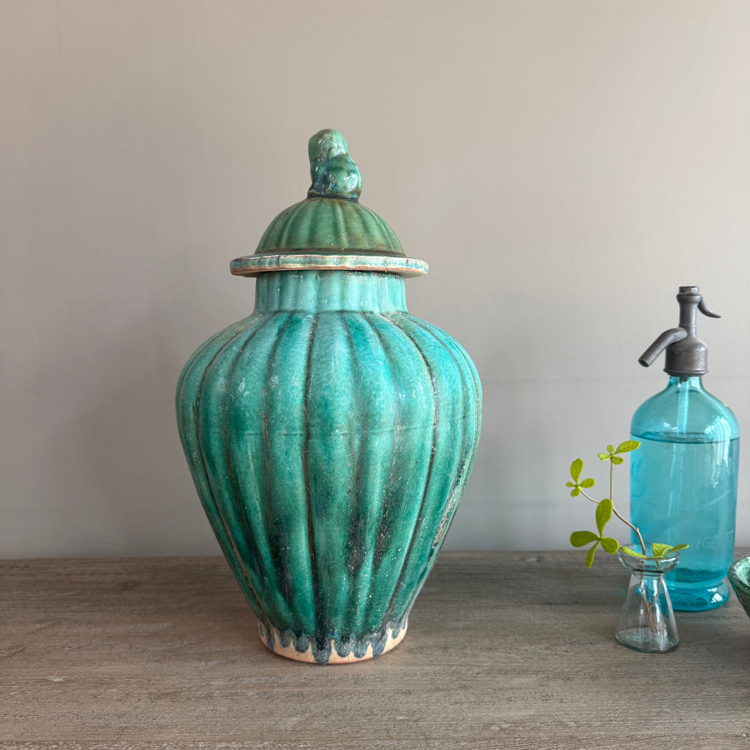 Green glazed stoneware temple jar with a rich crackle glaze and decorative bird finial, inspired by traditional Chinese ceramics and styled on a reclaimed wooden console.