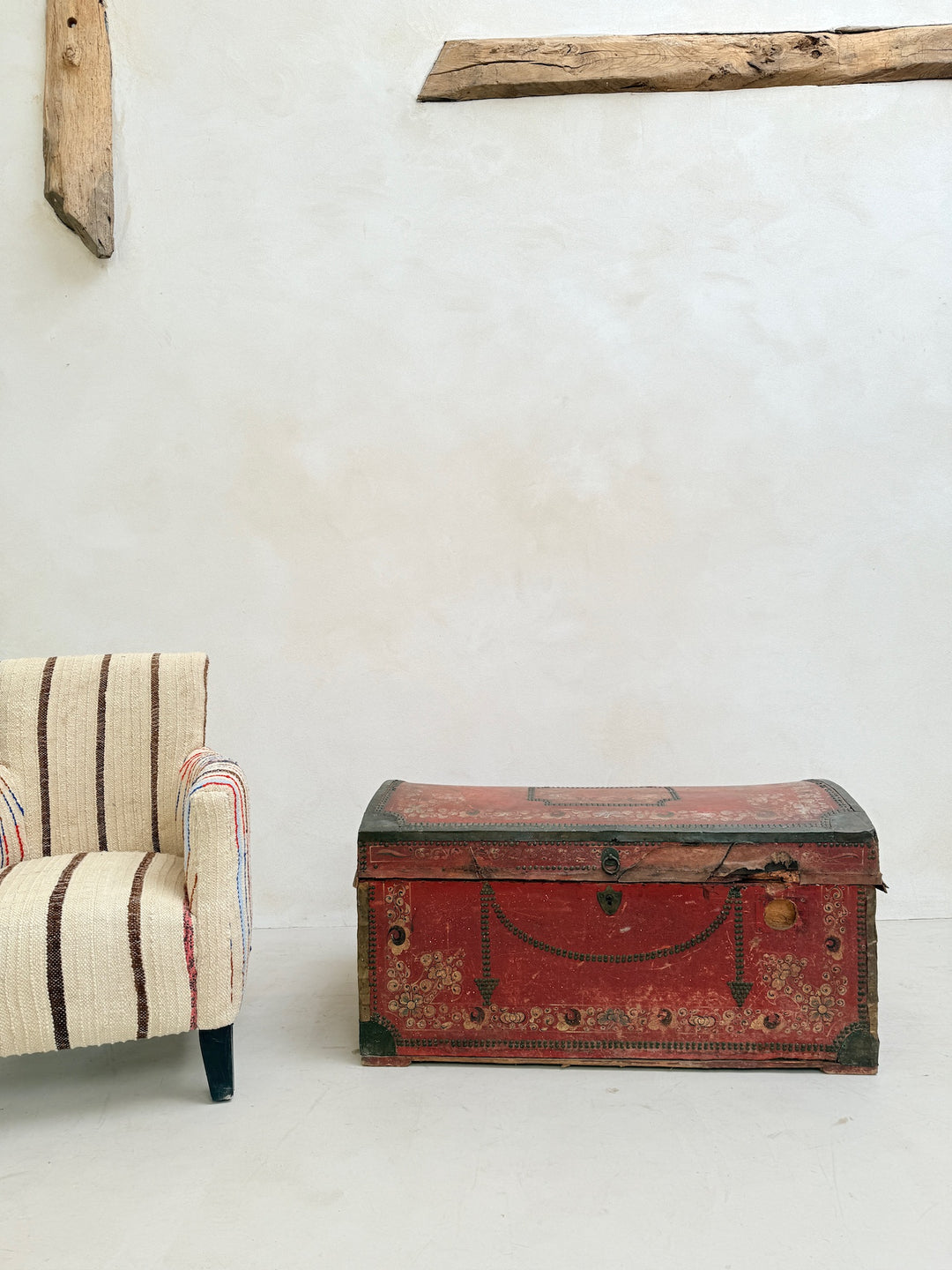 Red vintage trunk next to a striped armchair on a white background