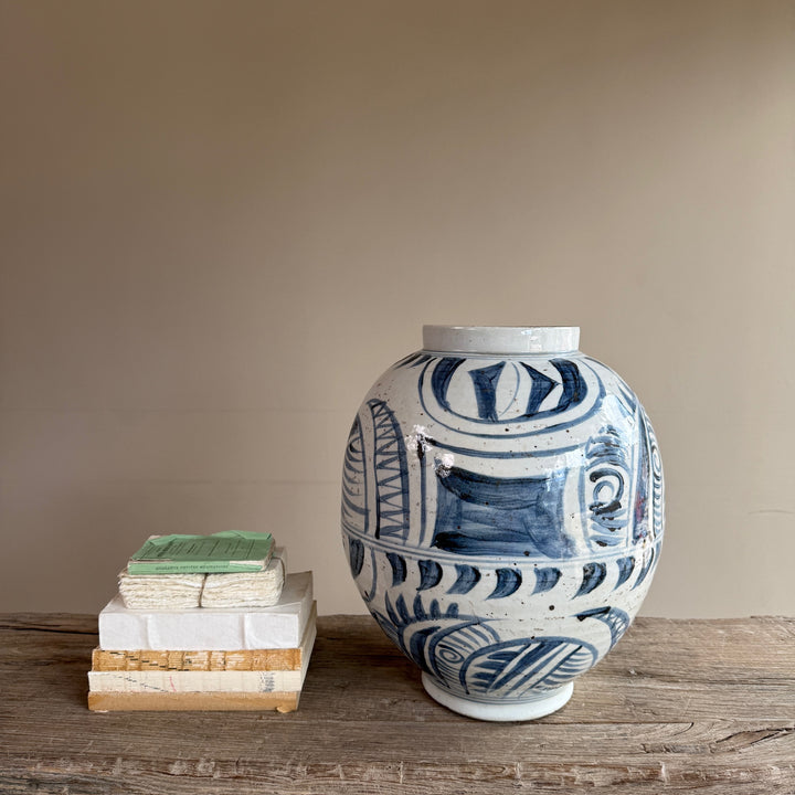 Hand-painted blue and white porcelain vase photographed beside stacked books to illustrate its generous proportions and decorative impact.
