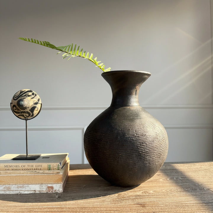brown vase with texture on table tope with books and antique spinning top