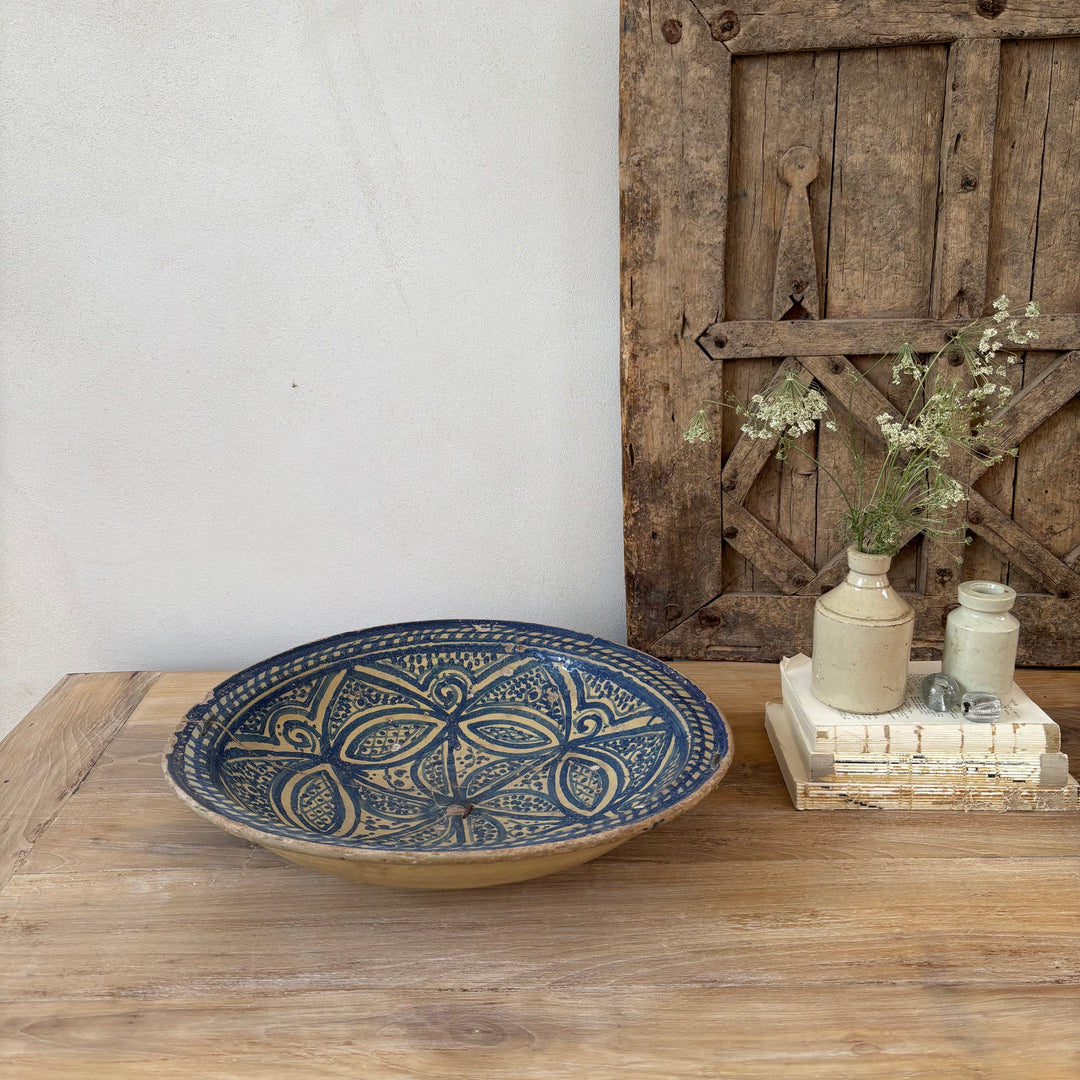 Decorative blue and beige ceramic bowl on a wooden surface with a rustic wooden door in the background.