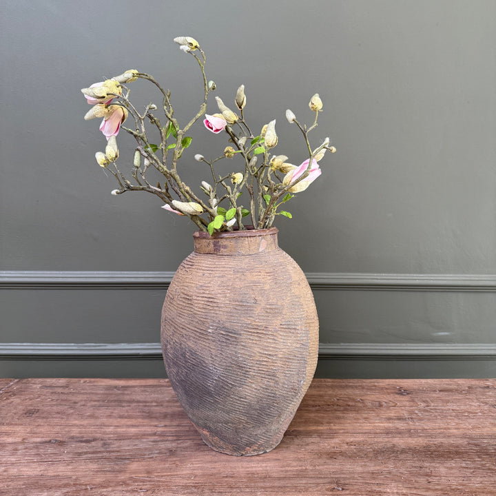 Large antique Chinese stoneware storage jar styled with flowering branches, showcasing its beautifully weathered patina and hand-combed surface in a contemporary country interior.
