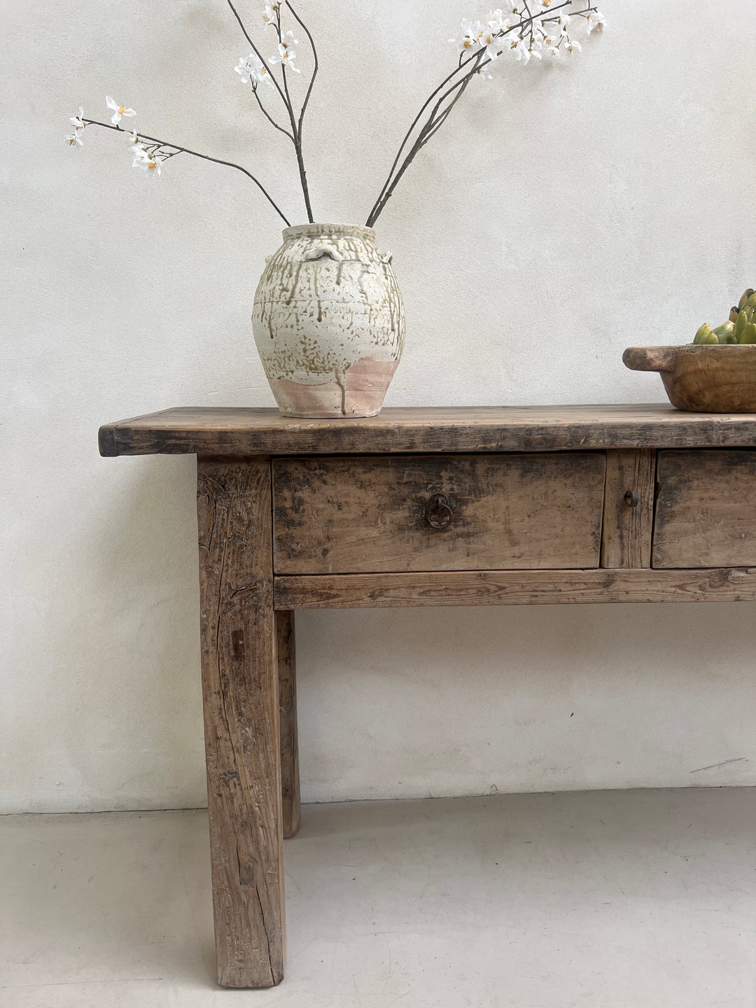 Wooden shelf against a light gray wall with a vase and branches.