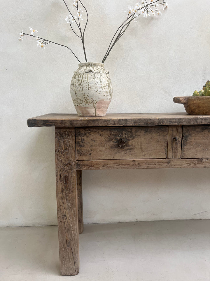 Wooden shelf against a light gray wall with a vase and branches.