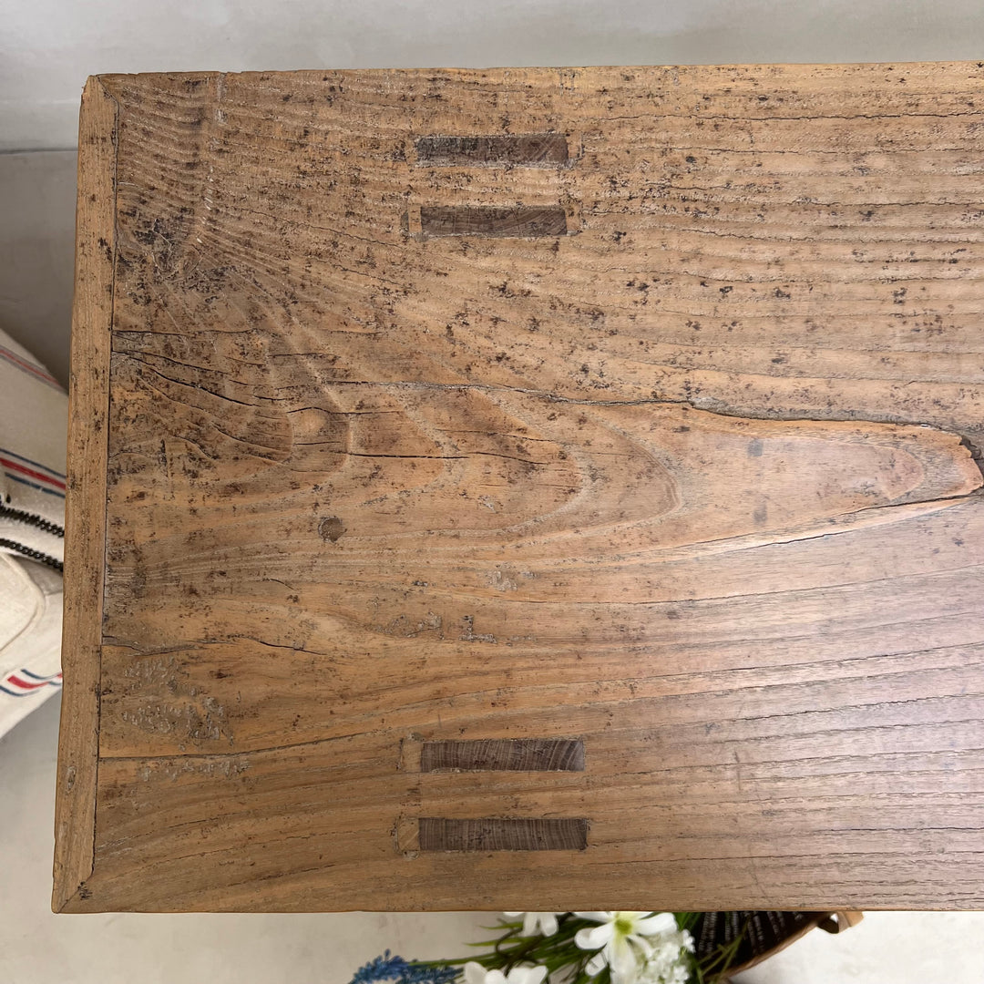 A close-up of a rustic wooden box or furniture piece showing the top surface with visible grain, knots, and dark recessed details.