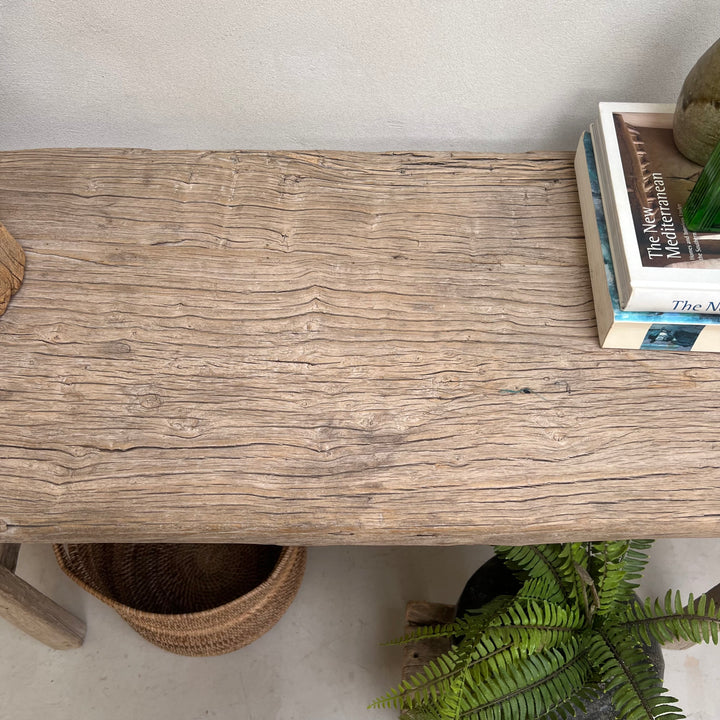 A rustic rectangular wooden console table with a weathered, textured gray-brown wood grain finish, styled with books, a plant, and a woven basket underneath.