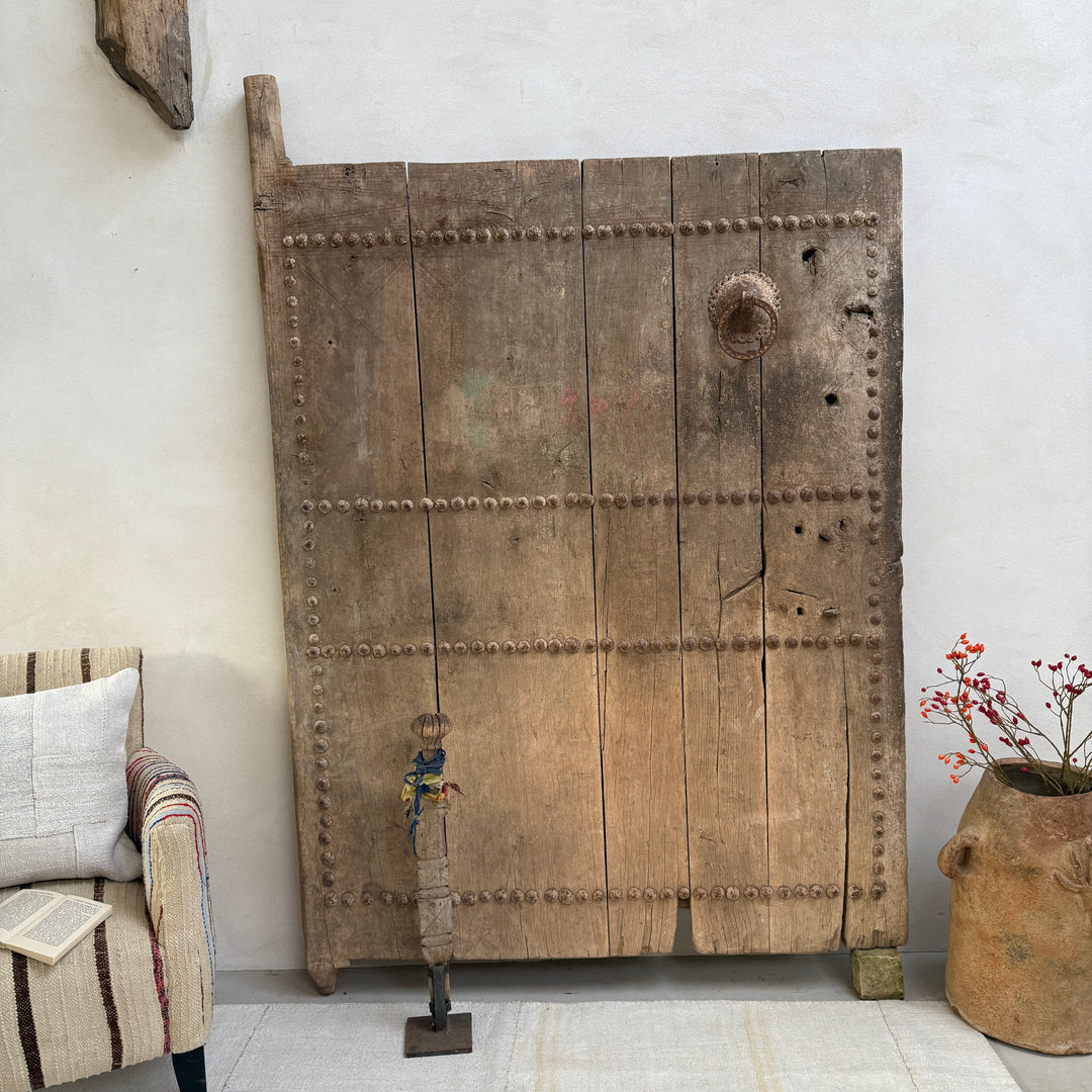 Large wooden door with nail details in a room with a chair and decorative elements.