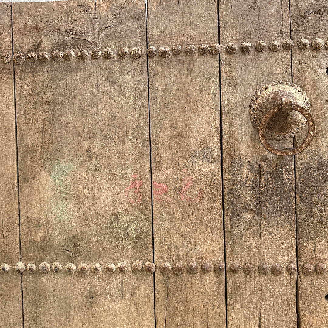 Close-up of a rustic wooden door with metal rivets and a handle.