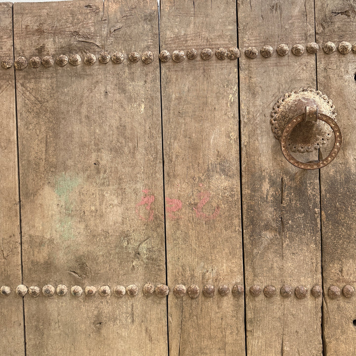 Close-up of a rustic wooden door with metal rivets and a handle.