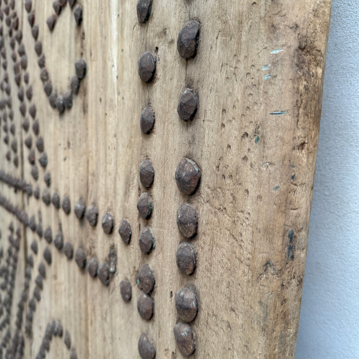 Wooden panel with metal studs arranged in a pattern against a gray background