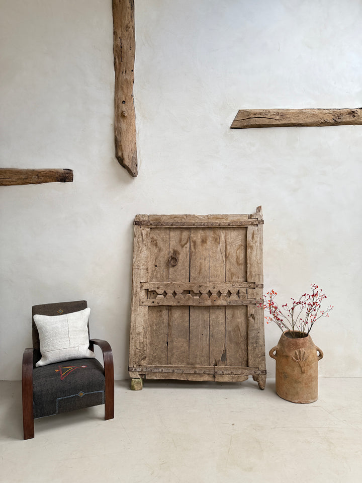 Vintage wooden panel on a wall with a rustic chair and decorative vase.