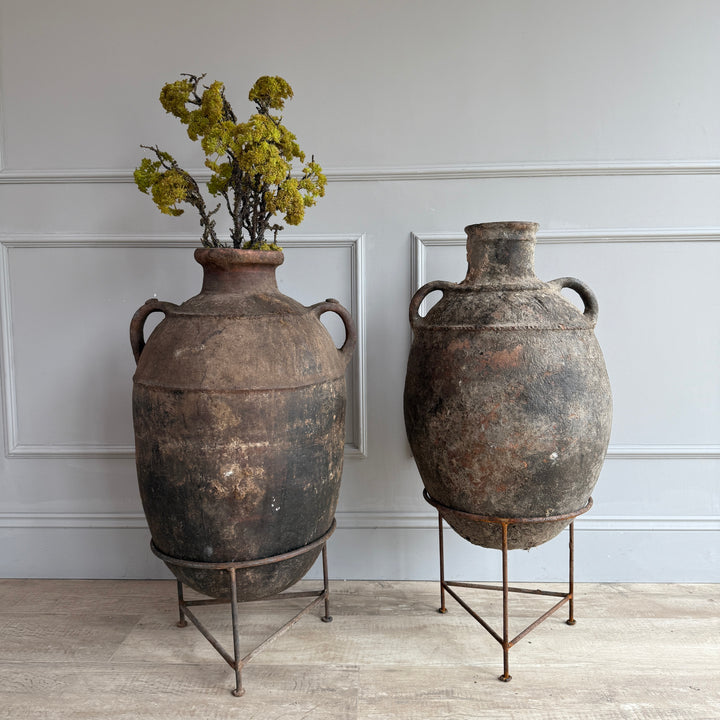 Two large rustic vases with a plant on a light gray background